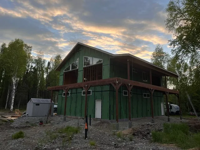 Two-story framed home wrapped in sheathing under a dramatic sky
